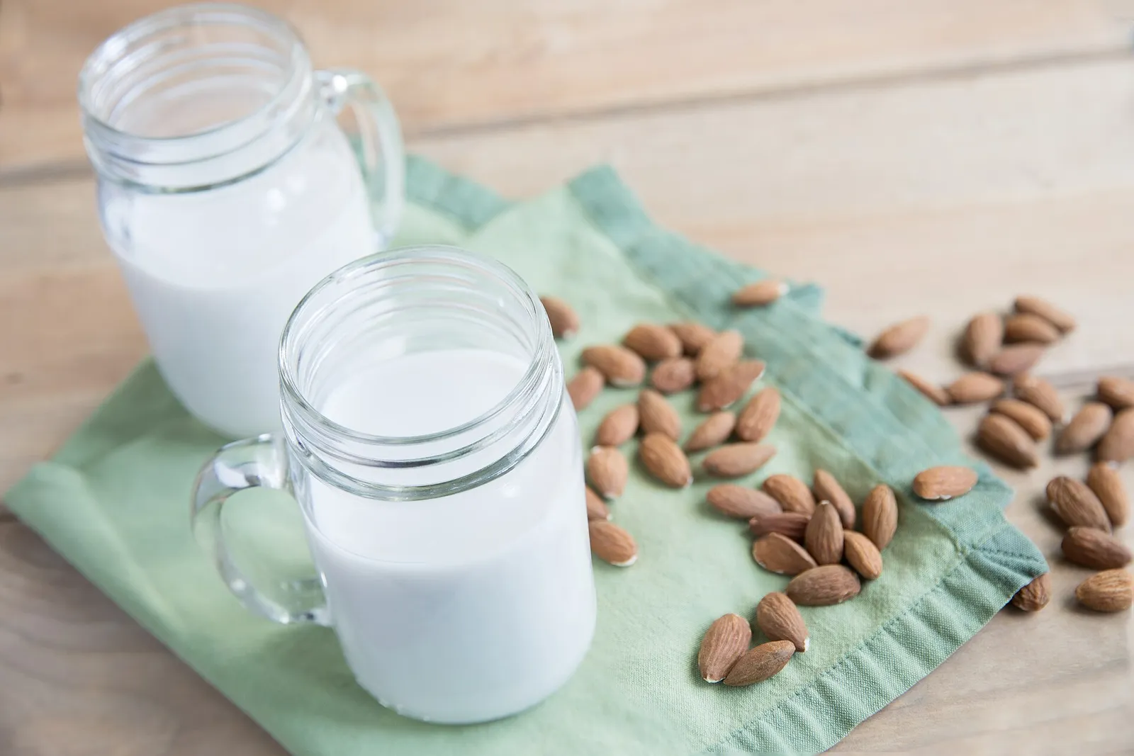 Un vaso de bebida vegetal de almendra junto a almendras sobre una mesa